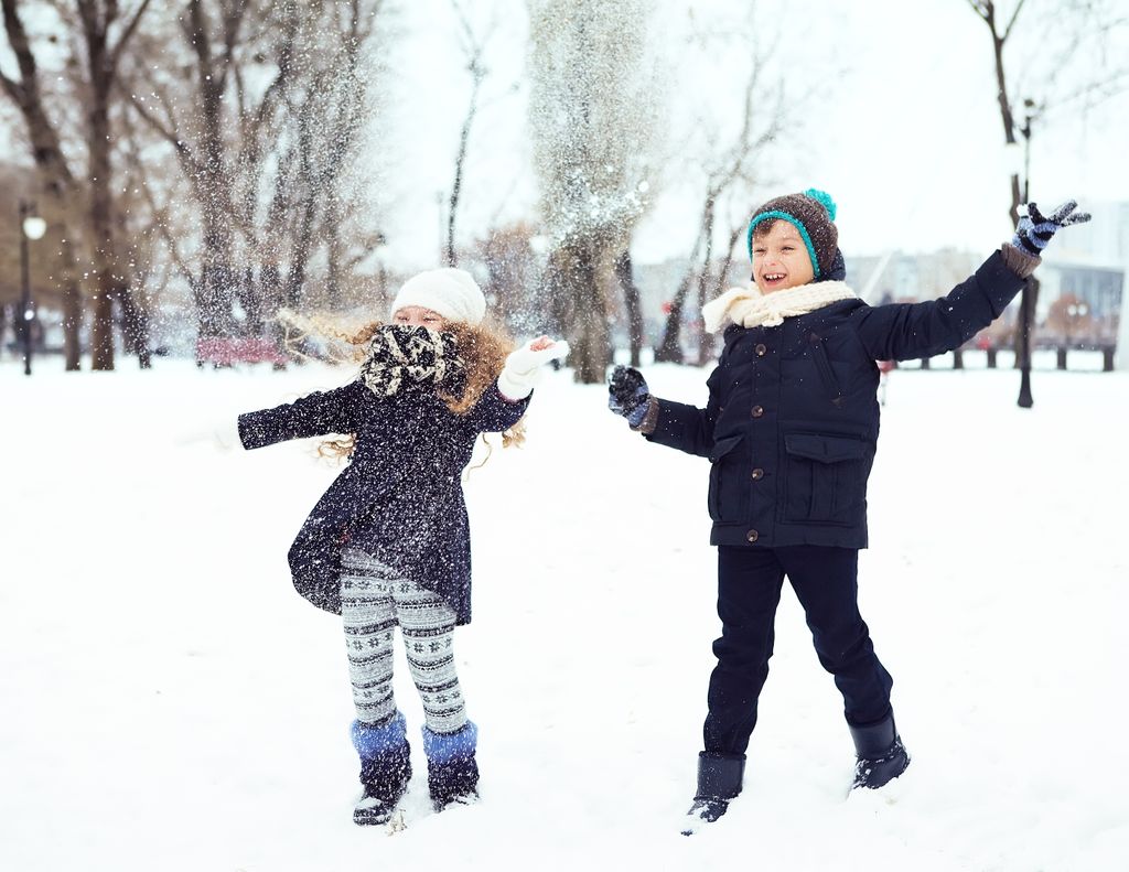 Two smiling children enjoying a fun day in the snow, dressed in winter clothing, playing outdoors.